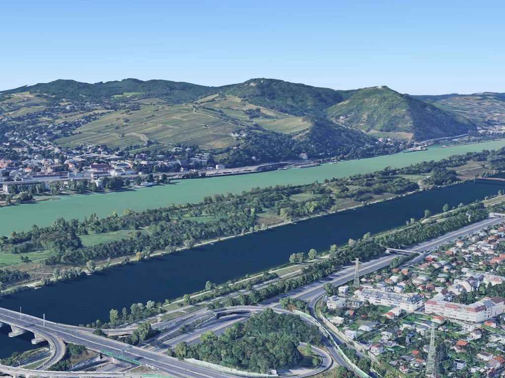 Luftbild von Wien: vorne Autobahn und Häuser, dann Neue Donau, Donauinsel und Donau, dahinter Weinberge und die bewaldeten Hügel von Döbling